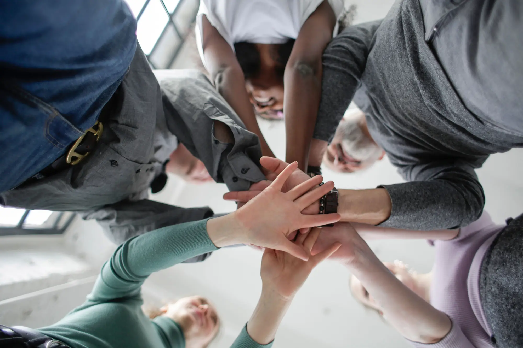 Équipe en cercle, vue d'en dessous, qui superpose ses mains en souriant