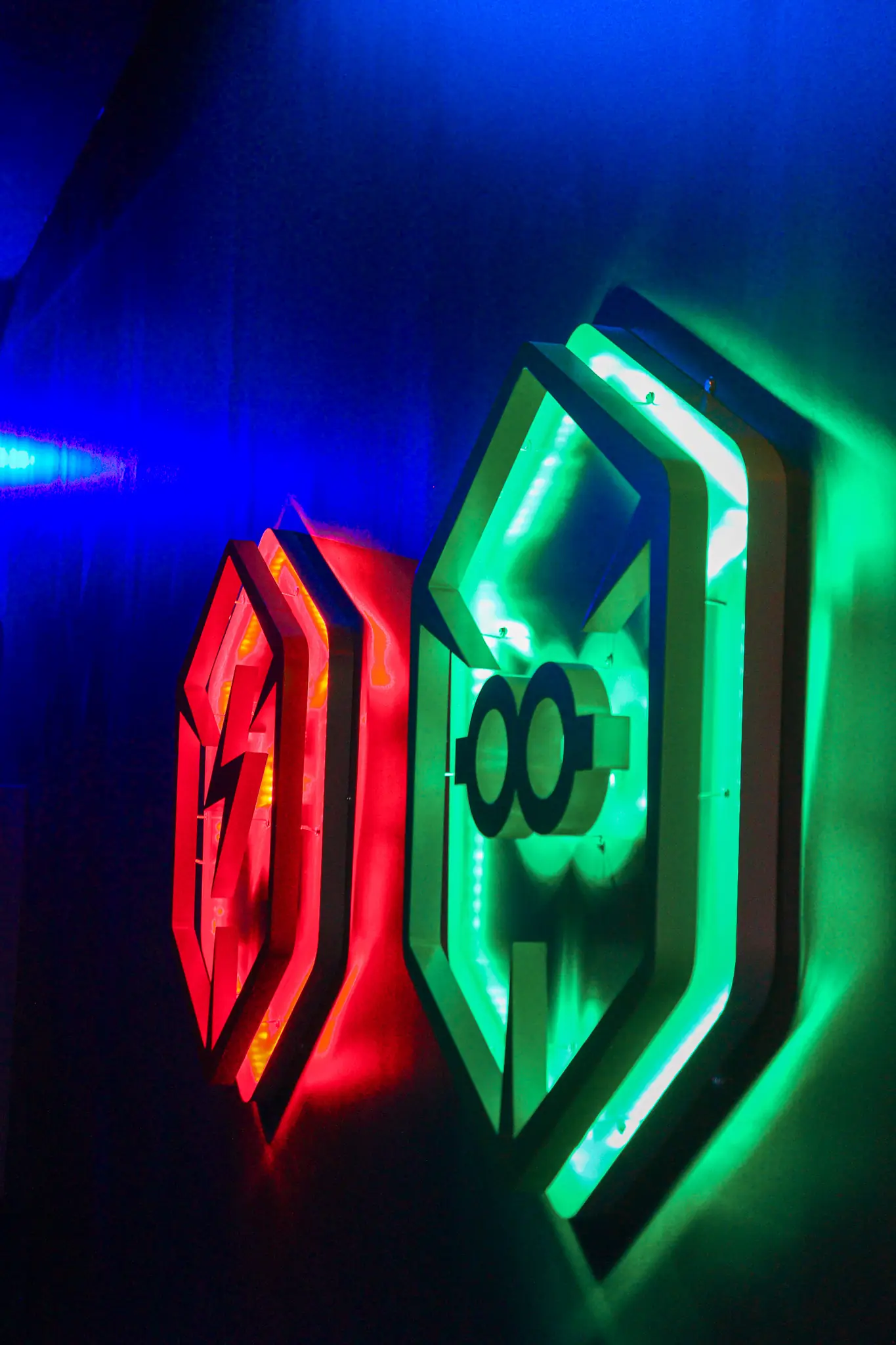 Logos lumineux du Cube Challenge en néon rouge et vert sur un mur bleu
